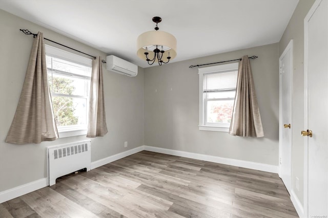 unfurnished room with a wall mounted air conditioner, radiator heating unit, light hardwood / wood-style floors, and a notable chandelier