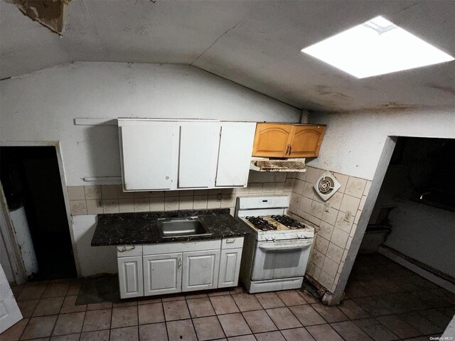 kitchen featuring lofted ceiling with skylight, white range with gas cooktop, sink, white cabinetry, and light tile patterned flooring