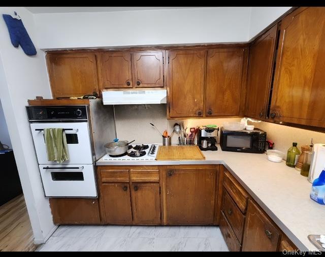 kitchen featuring brown cabinets, marble finish floor, under cabinet range hood, white appliances, and light countertops