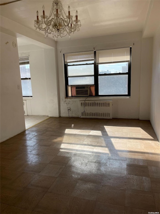 empty room featuring radiator heating unit, cooling unit, and a notable chandelier