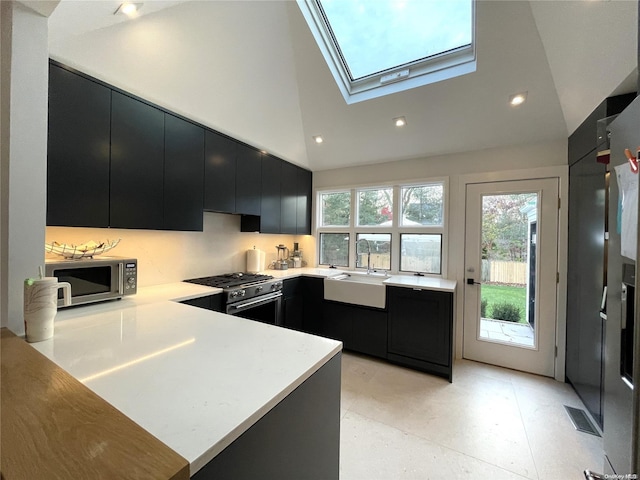 kitchen featuring high vaulted ceiling, sink, a skylight, kitchen peninsula, and stainless steel appliances