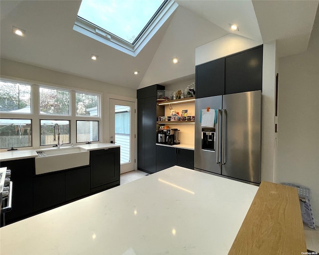 kitchen with a skylight, sink, high vaulted ceiling, stainless steel fridge, and a kitchen island