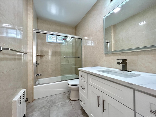 full bathroom featuring vanity, shower / bath combination with glass door, tile patterned floors, tile walls, and radiator heating unit