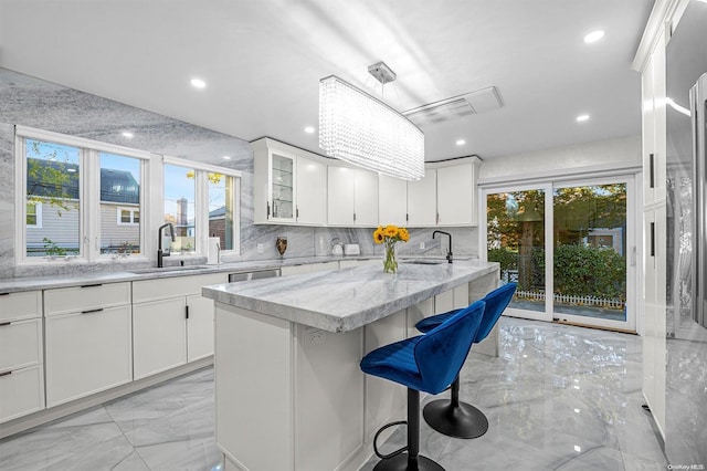 kitchen featuring a wealth of natural light, sink, white cabinets, and a kitchen island with sink