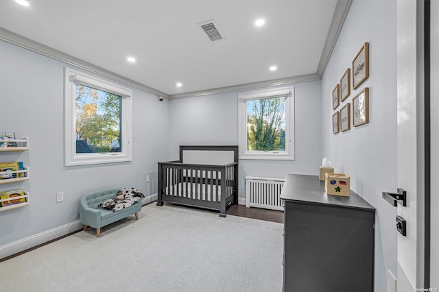 bedroom featuring a crib, crown molding, radiator, and multiple windows