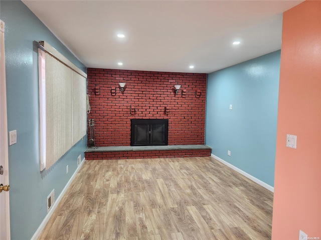 unfurnished living room featuring light hardwood / wood-style floors, a brick fireplace, and brick wall