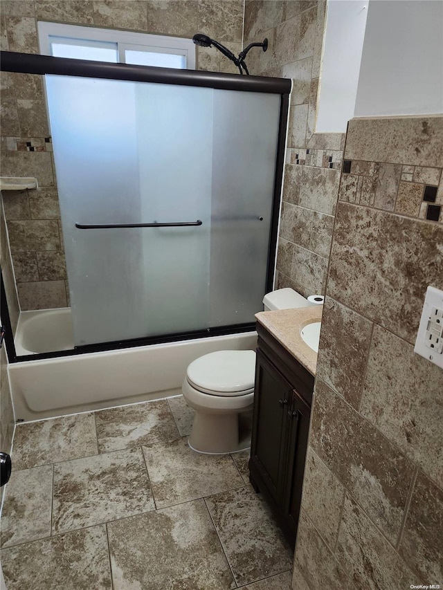 full bathroom featuring vanity, toilet, tile walls, and bath / shower combo with glass door