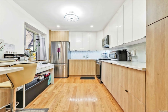 kitchen with light brown cabinets, white cabinets, sink, appliances with stainless steel finishes, and light hardwood / wood-style floors