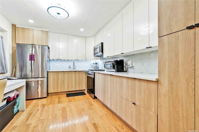 kitchen featuring white cabinets, backsplash, light hardwood / wood-style floors, and stainless steel appliances