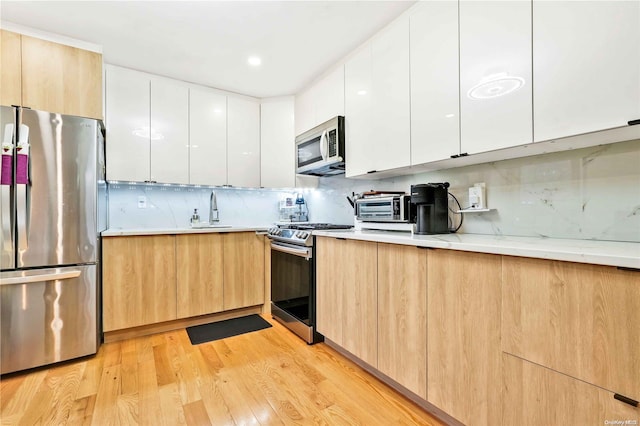 kitchen featuring sink, stainless steel appliances, white cabinetry, and light hardwood / wood-style flooring