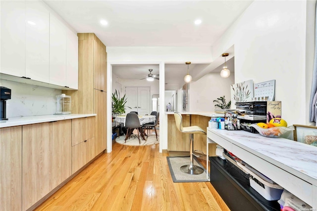 kitchen featuring white cabinets, hanging light fixtures, ceiling fan, decorative backsplash, and light hardwood / wood-style floors