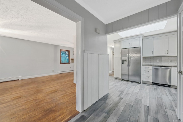 kitchen with stainless steel appliances, a baseboard radiator, a textured ceiling, decorative backsplash, and light wood-type flooring