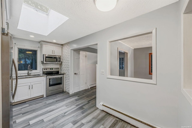 kitchen with sink, white cabinetry, stainless steel appliances, and a skylight