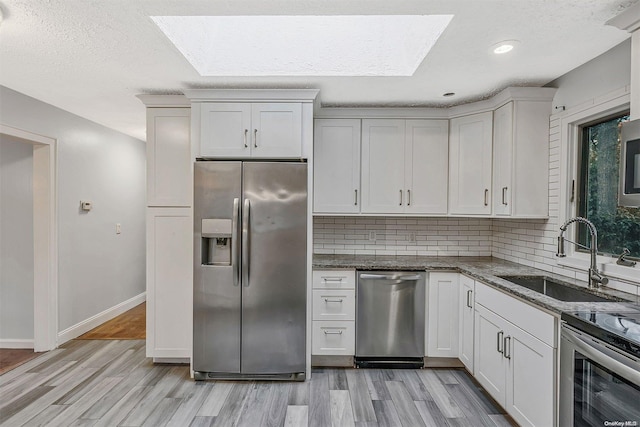 kitchen featuring light wood-type flooring, sink, appliances with stainless steel finishes, and a skylight