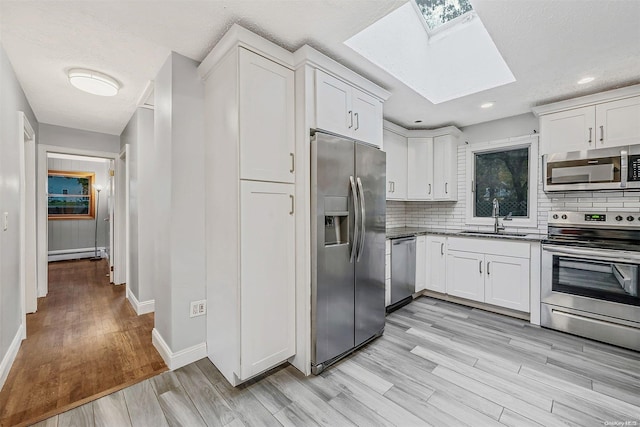 kitchen with white cabinets, sink, appliances with stainless steel finishes, and a skylight