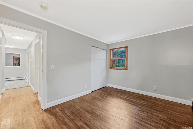 empty room with hardwood / wood-style floors, a baseboard radiator, and crown molding