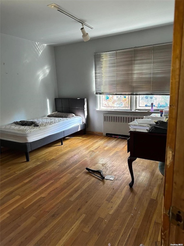 bedroom with radiator, rail lighting, and hardwood / wood-style flooring