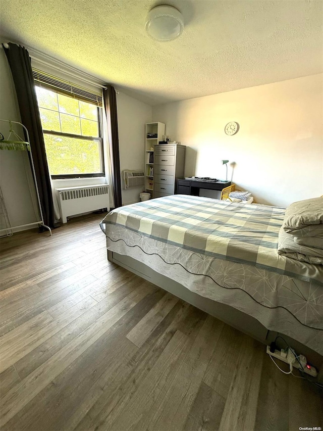 unfurnished bedroom with hardwood / wood-style flooring, radiator heating unit, a textured ceiling, and an AC wall unit