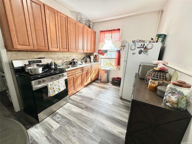 kitchen with light wood-type flooring, stainless steel gas stove, tasteful backsplash, and sink