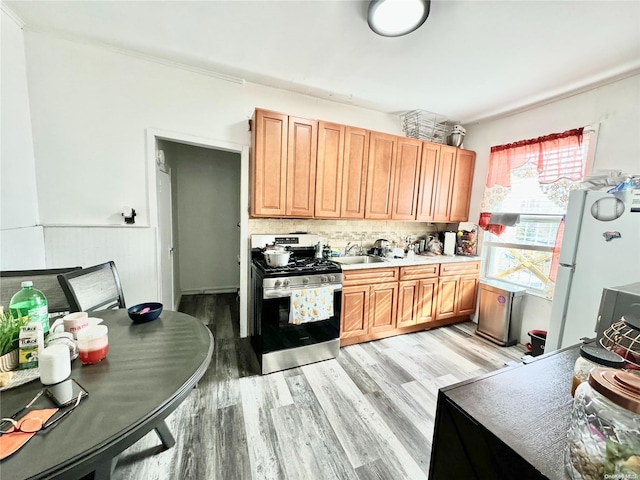 kitchen with tasteful backsplash, white fridge, light hardwood / wood-style flooring, and stainless steel gas range oven