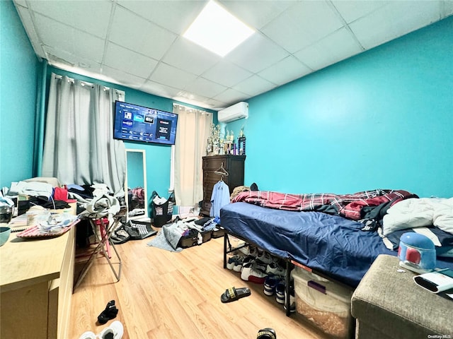 bedroom with wood-type flooring, a paneled ceiling, and a wall mounted AC