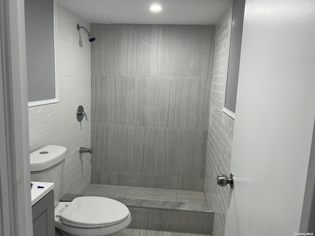 bathroom featuring a tile shower, vanity, tile walls, and toilet