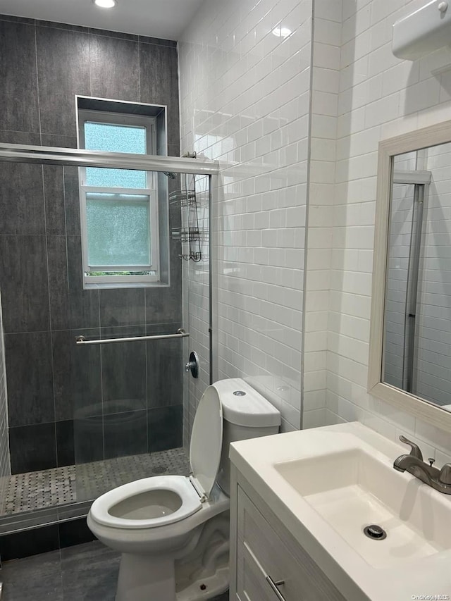 bathroom with an enclosed shower, vanity, tile walls, tile patterned flooring, and toilet