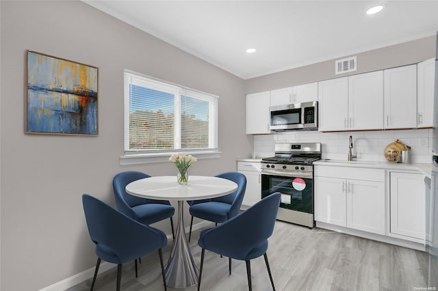 kitchen with backsplash, sink, light wood-type flooring, appliances with stainless steel finishes, and white cabinetry