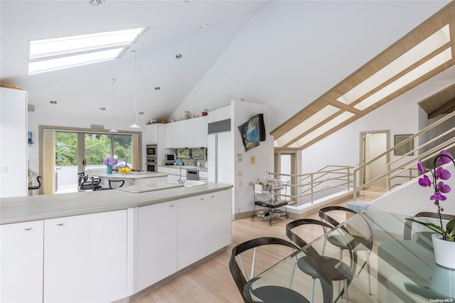 kitchen featuring light wood-type flooring, high vaulted ceiling, white cabinetry, and a skylight