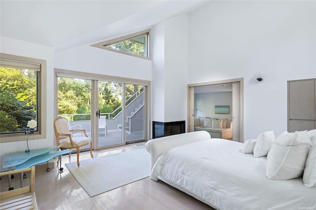 bedroom with access to exterior, a high ceiling, hardwood / wood-style flooring, and multiple windows