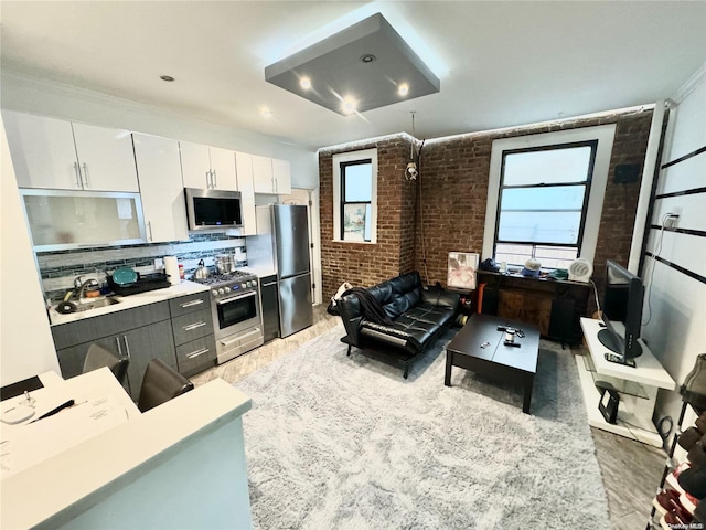 interior space featuring backsplash, white cabinets, sink, appliances with stainless steel finishes, and brick wall