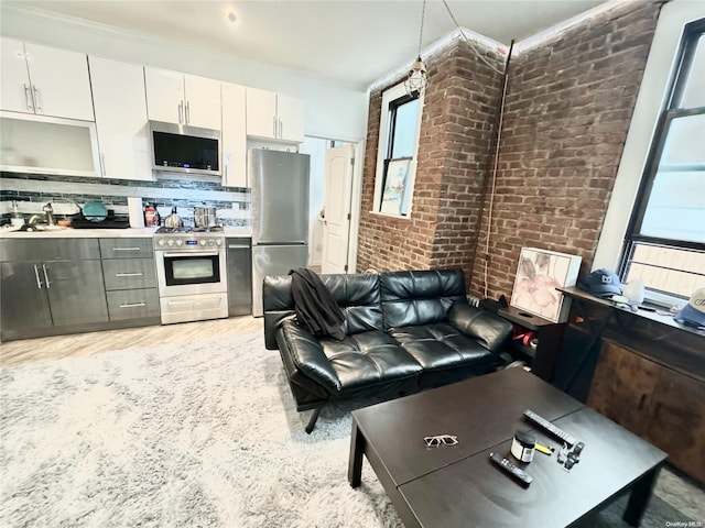 kitchen featuring appliances with stainless steel finishes, brick wall, crown molding, sink, and white cabinets