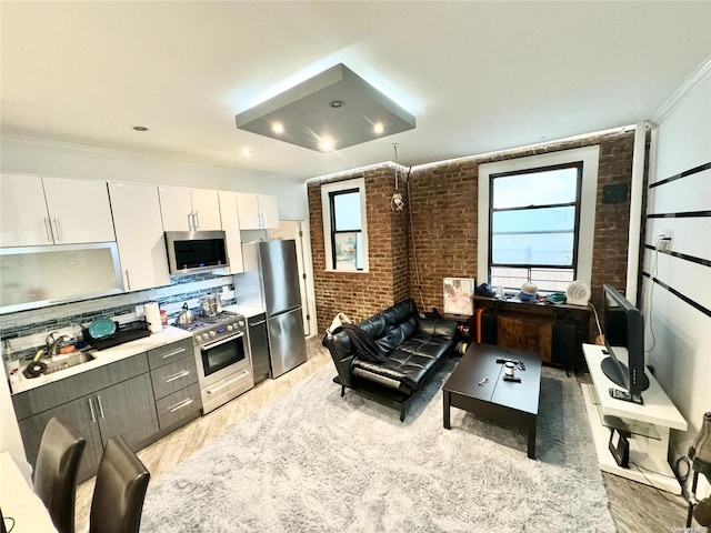 kitchen with white cabinets, sink, light wood-type flooring, stainless steel appliances, and brick wall