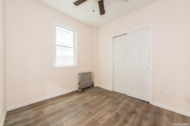 unfurnished bedroom featuring a closet, ceiling fan, radiator heating unit, and dark hardwood / wood-style floors