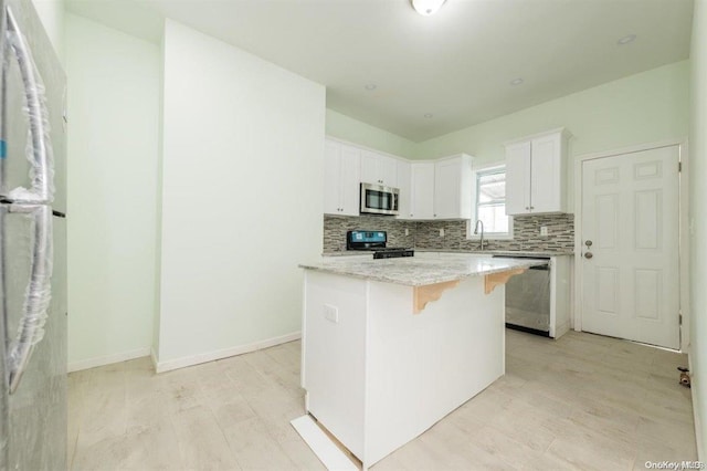 kitchen featuring appliances with stainless steel finishes, light stone counters, light hardwood / wood-style flooring, white cabinets, and a kitchen island