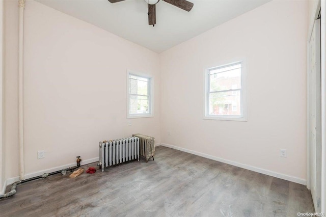 empty room featuring ceiling fan, radiator, and light hardwood / wood-style flooring