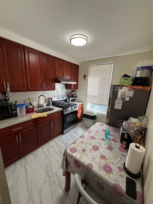 kitchen featuring under cabinet range hood, a sink, marble finish floor, appliances with stainless steel finishes, and reddish brown cabinets