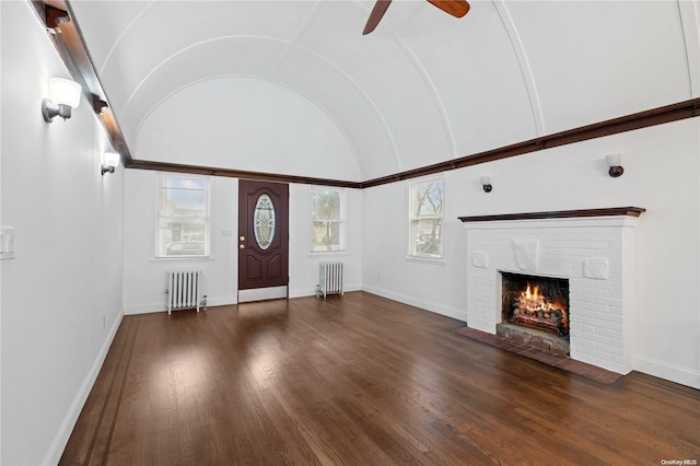 unfurnished living room with radiator heating unit, dark hardwood / wood-style floors, a brick fireplace, and lofted ceiling