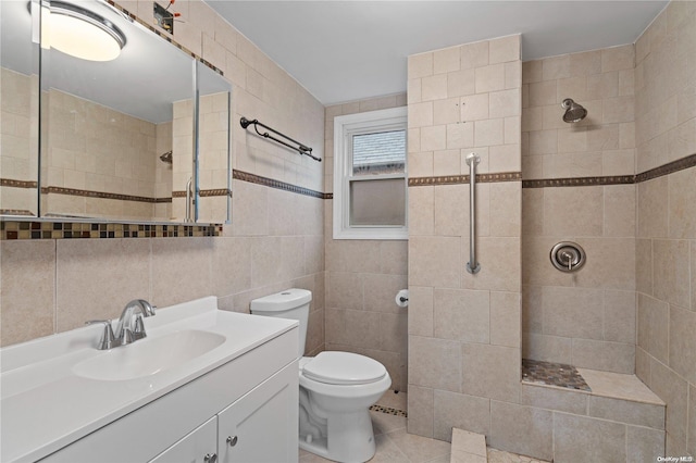 bathroom with a tile shower, tile patterned floors, toilet, vanity, and tile walls