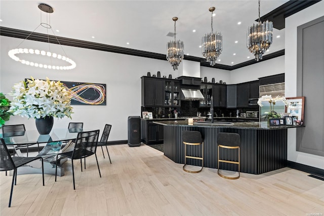 kitchen with decorative light fixtures, light hardwood / wood-style floors, a kitchen bar, and wall chimney range hood