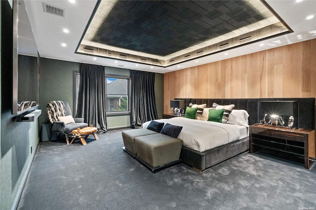 bedroom with carpet floors, wooden walls, and a tray ceiling