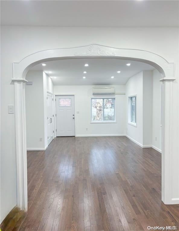 unfurnished living room featuring ornate columns, dark hardwood / wood-style flooring, and a wall mounted air conditioner