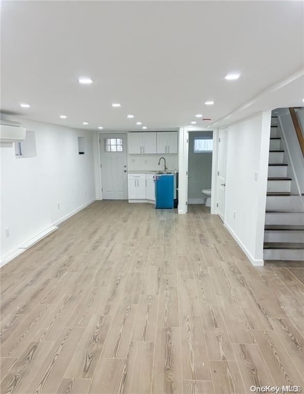 basement featuring light hardwood / wood-style floors, sink, and a wall mounted AC