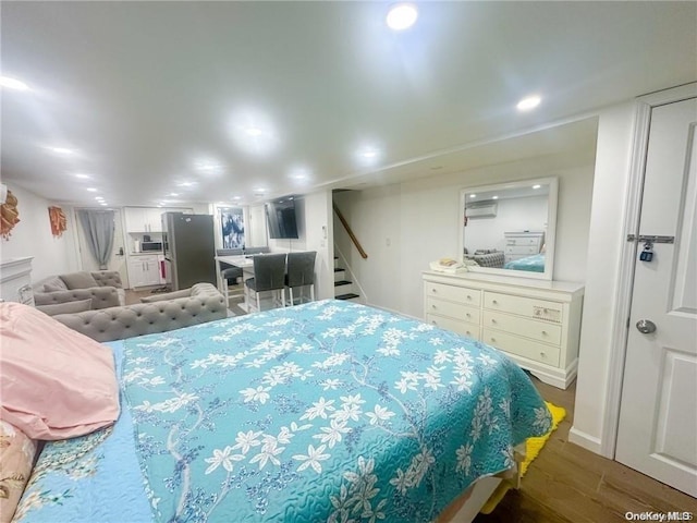 bedroom with a wall mounted air conditioner, dark hardwood / wood-style floors, and stainless steel refrigerator