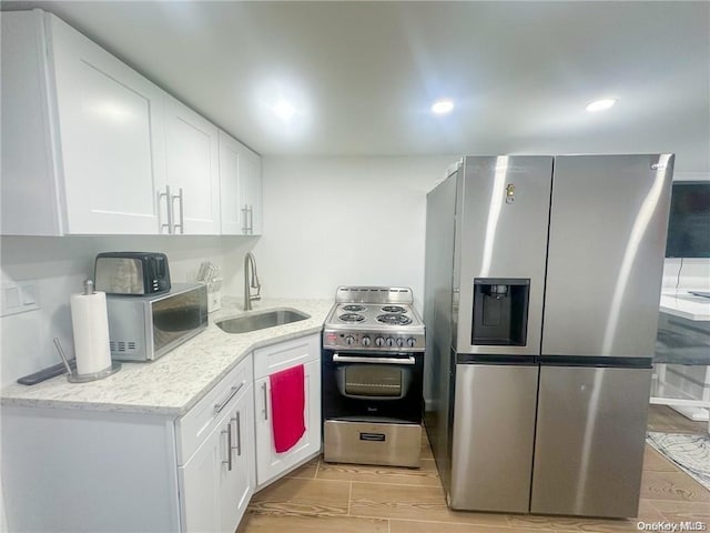 kitchen with light stone counters, stainless steel appliances, sink, white cabinets, and light hardwood / wood-style floors