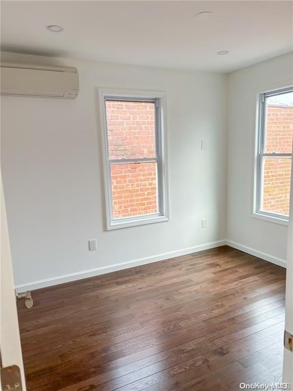 empty room with dark hardwood / wood-style flooring and an AC wall unit