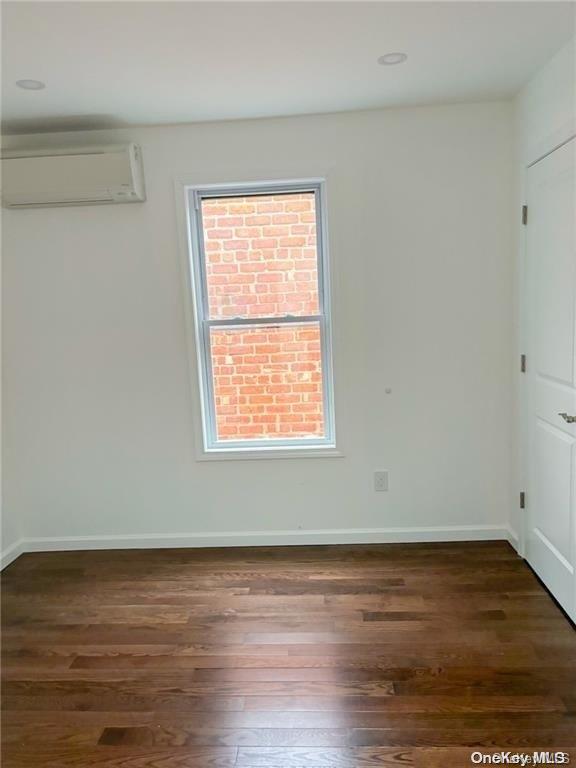 empty room featuring a wall unit AC and dark hardwood / wood-style floors