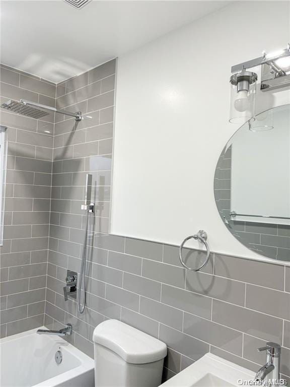 bathroom with toilet, tile walls, and tiled shower / bath