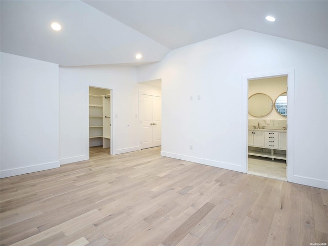 unfurnished bedroom featuring a walk in closet, vaulted ceiling, connected bathroom, light hardwood / wood-style floors, and a closet