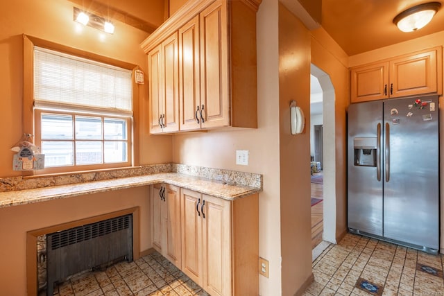 kitchen featuring light brown cabinets, light stone countertops, radiator heating unit, and stainless steel refrigerator with ice dispenser